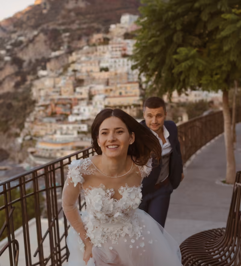 A bride and groom running along a hillside village path