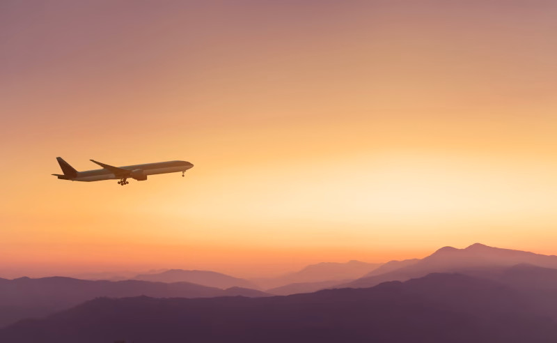 A passenger plane climbing into an orange sunset sky