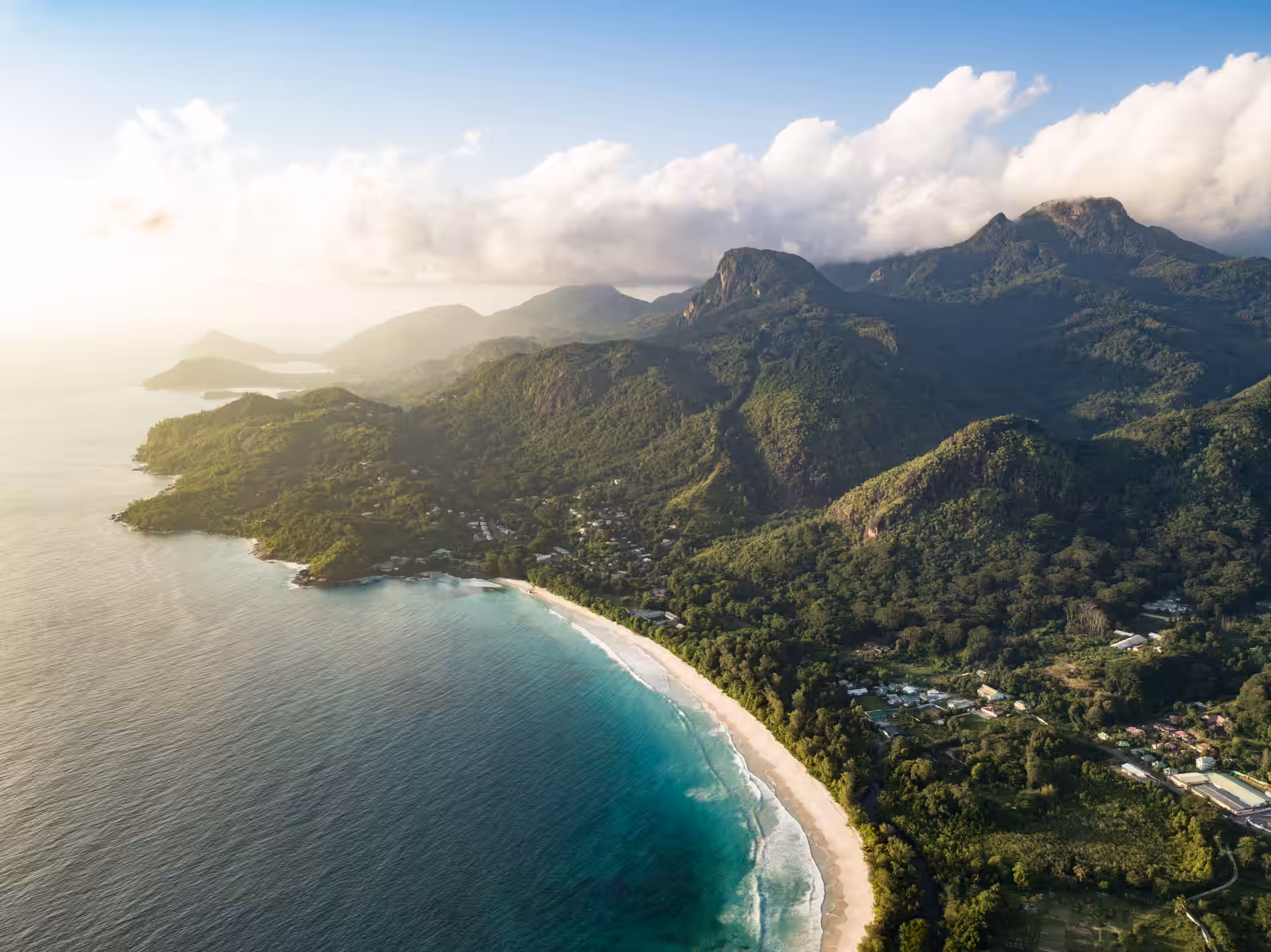 A tree covered mountain rain with a sandy bay and a clear blue sea